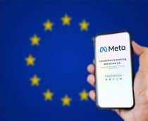 Ao fundo, desfocada, a bandeira da União Europeia; à direita, pessoa segurando um smartphone, no qual é exibida uma página da Meta