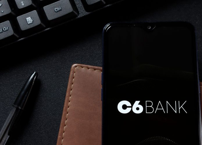 Foto de um celular com o logo da C6 Bank, uma caneta e uma carteira