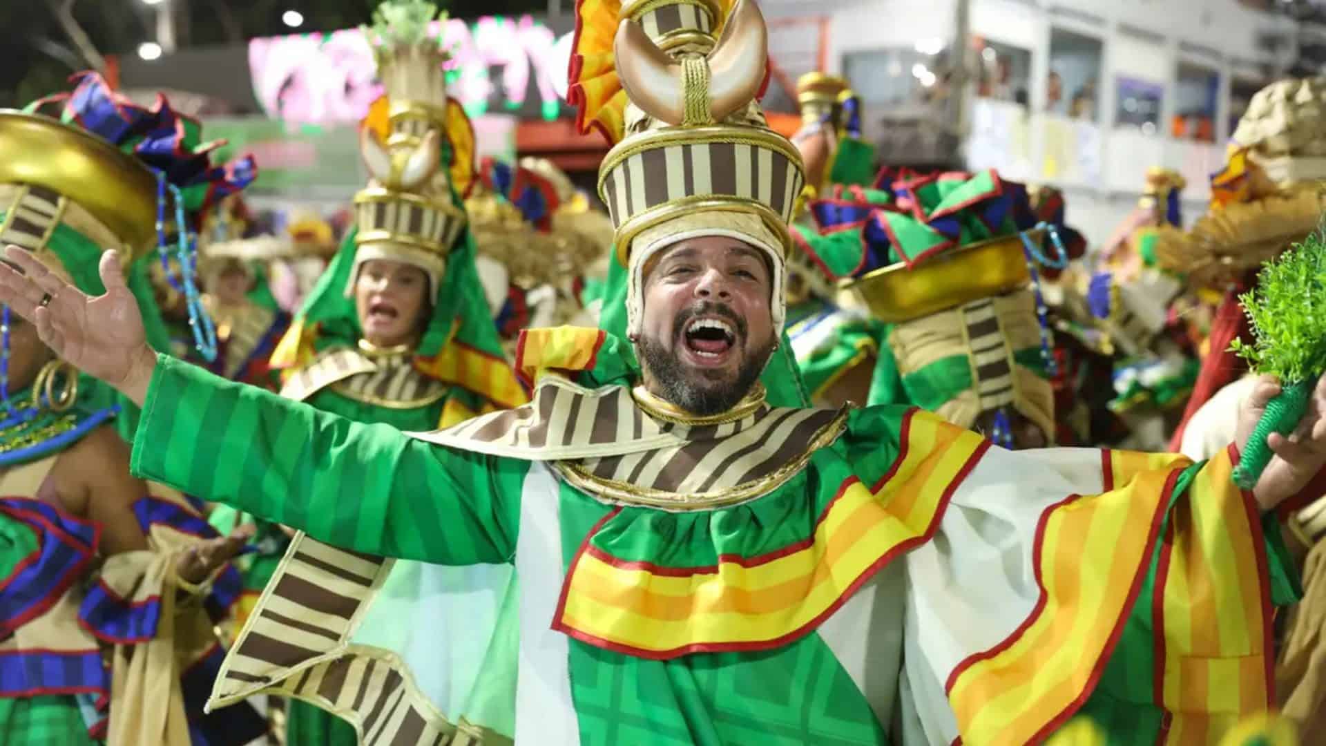 Homem sorrindo de braços abertos durante desfile de escola de samba no Rio de Janeiro no Carnaval de 2025
