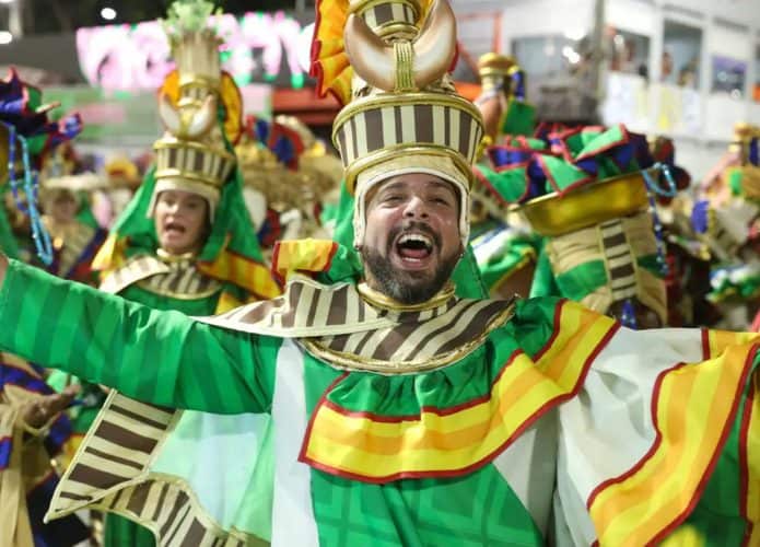 Homem sorrindo de braços abertos durante desfile de escola de samba no Rio de Janeiro no Carnaval de 2025
