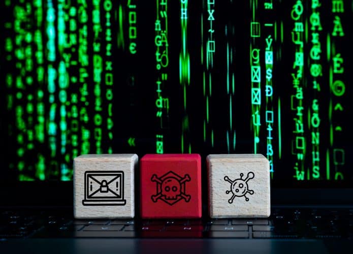 Cubinhos com desenhos de vírus, perigo e desinformação colocados em cima de teclado de notebook cuja tela mostra imagem de caracteres verdes na vertical estilo Matrix