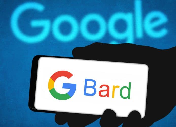 Pessoa segurando celular exibindo logomarca do Bard na tela; aparelho está na frente de tela com letreiro do Google em azul