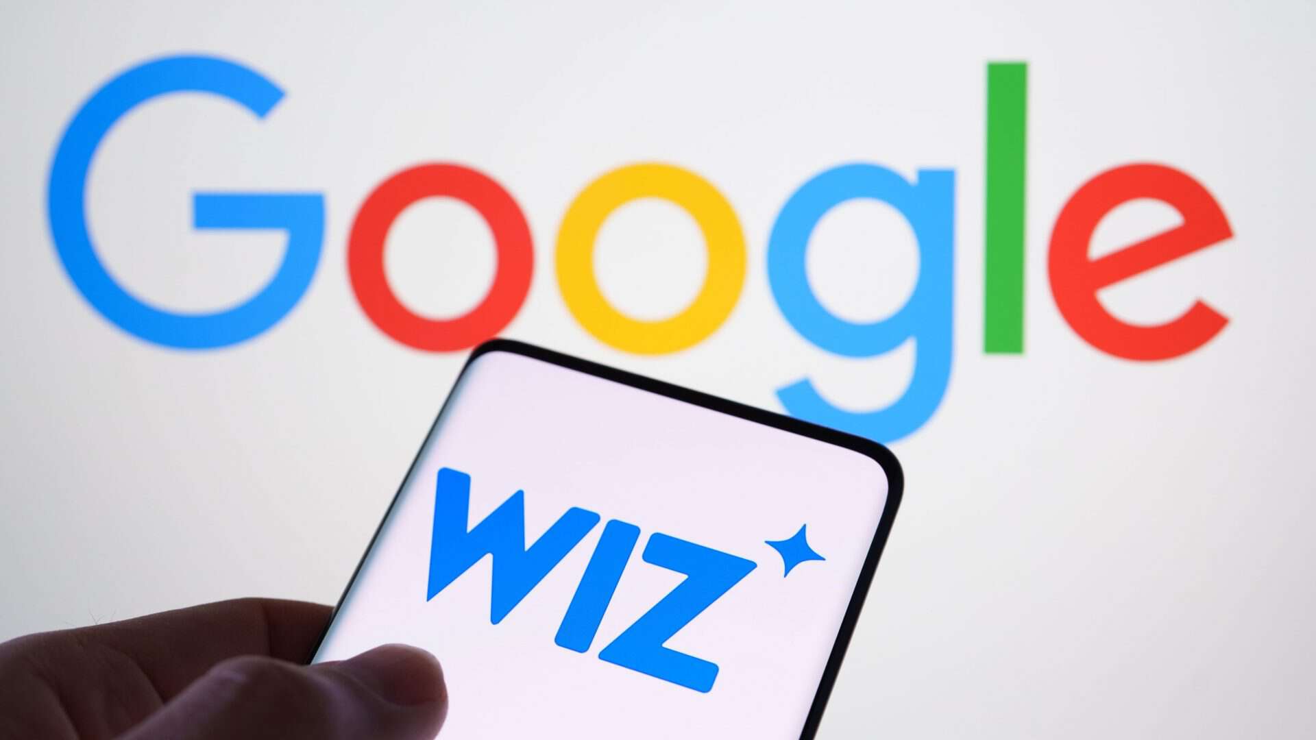 Pessoa segurando celular com logomarca da Wiz na tela colocado na frente de tela exibindo logomarca do Google