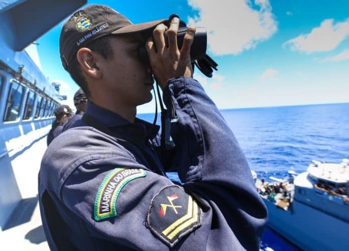 Militar da Marinha olhando por binóculos na beira de um barco em alto-mar