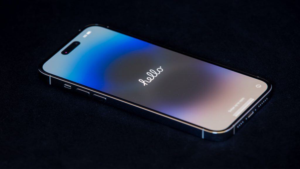 Tela de boas vindas num iPhone 16 Pro Max colocado em cima de superfície preta