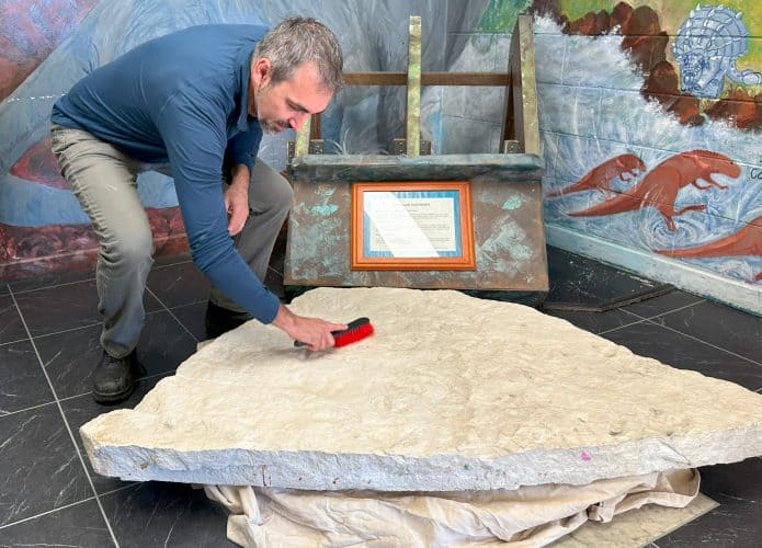 Dr Romilio escovando pedra com pegadas de dinossauro na Austrália