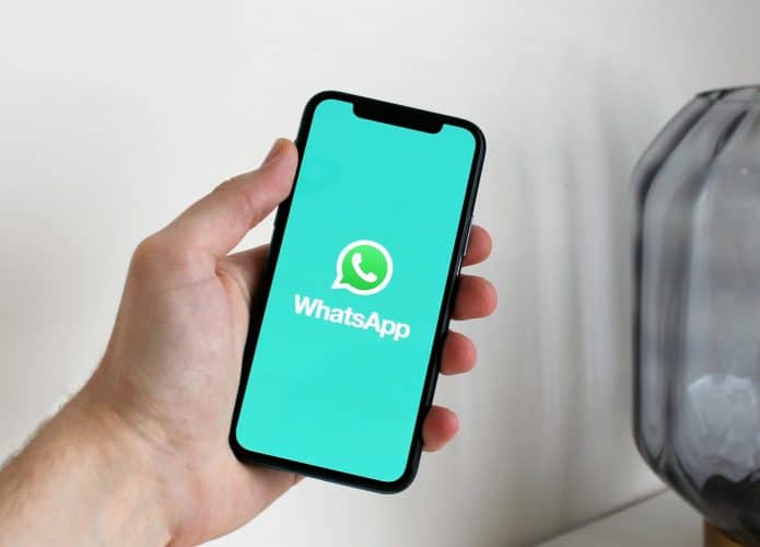 Mão segurando celular com logo do WhatsApp