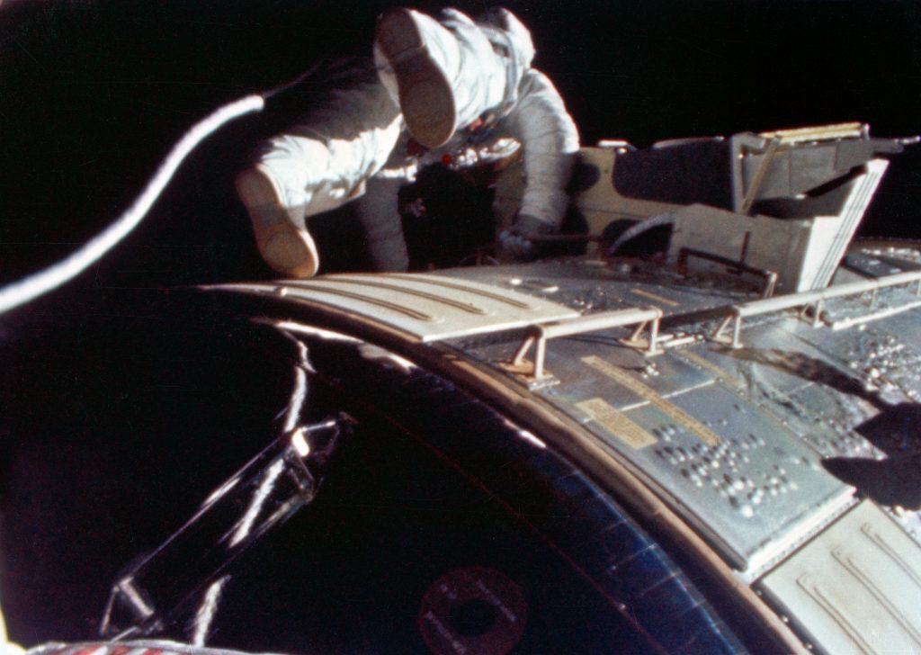 Imagem do astronauta Alfred Worden flutuando no espaço durante a missão Apollo 15, capturada a cerca de 340 mil quilômetros da Terra. Ele aparece fora da cápsula realizando tarefas científicas no módulo de instrumentos, com o fundo escuro do espaço ao redor.
