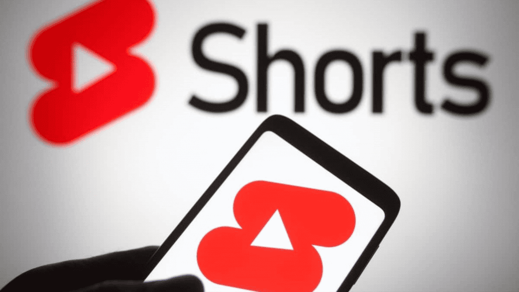 Pessoa segurando celular com logo do YouTube Shorts na tela, também exibido numa tela ao fundo