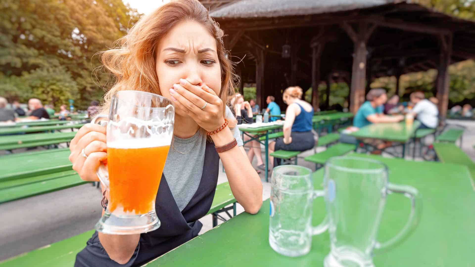 Mulher bebendo um copo de cerveja com uma expressão de desgostos