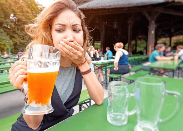 Mulher bebendo um copo de cerveja com uma expressão de desgostos