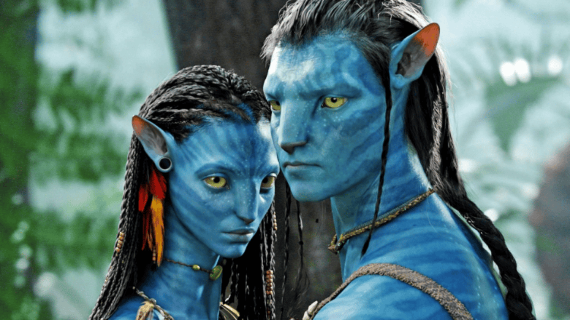 Cena do filme Avatar com dois personagens da espécie Na’vi, de pele azul e olhos amarelos, em um ambiente de floresta exuberante. Eles estão próximos, com expressões sérias e detalhes tribais no rosto e vestimentas.