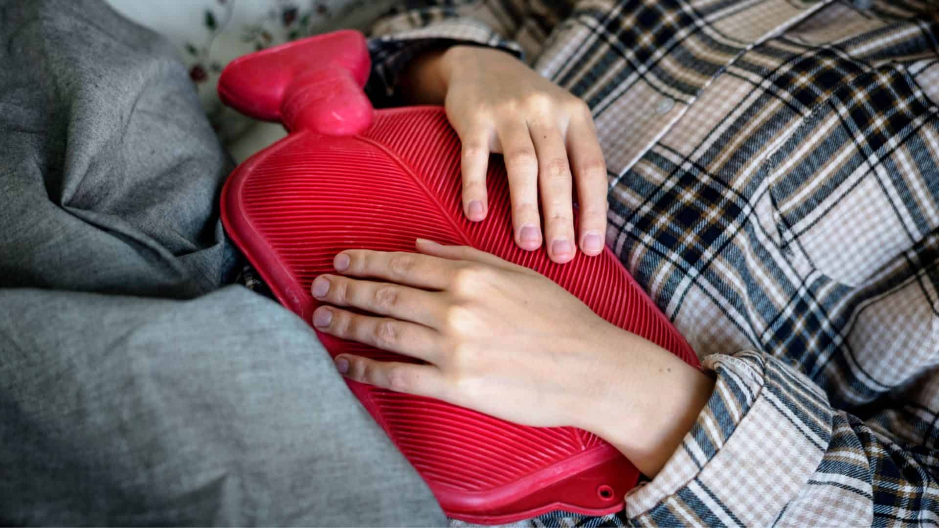 mulher com bolsa de água quente na barriga com cólica