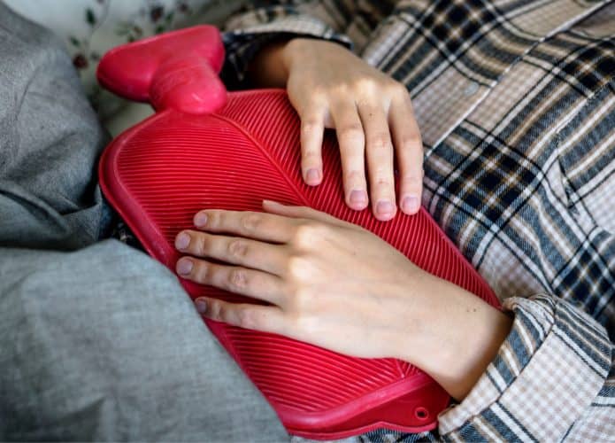 mulher com bolsa de água quente na barriga com cólica