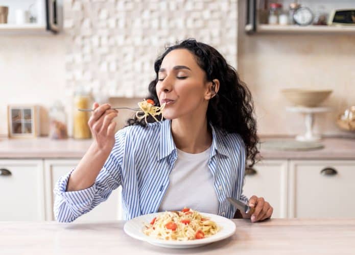 imagem mostra uma mulher aproveitando cada momento de sua refeição: macarronada