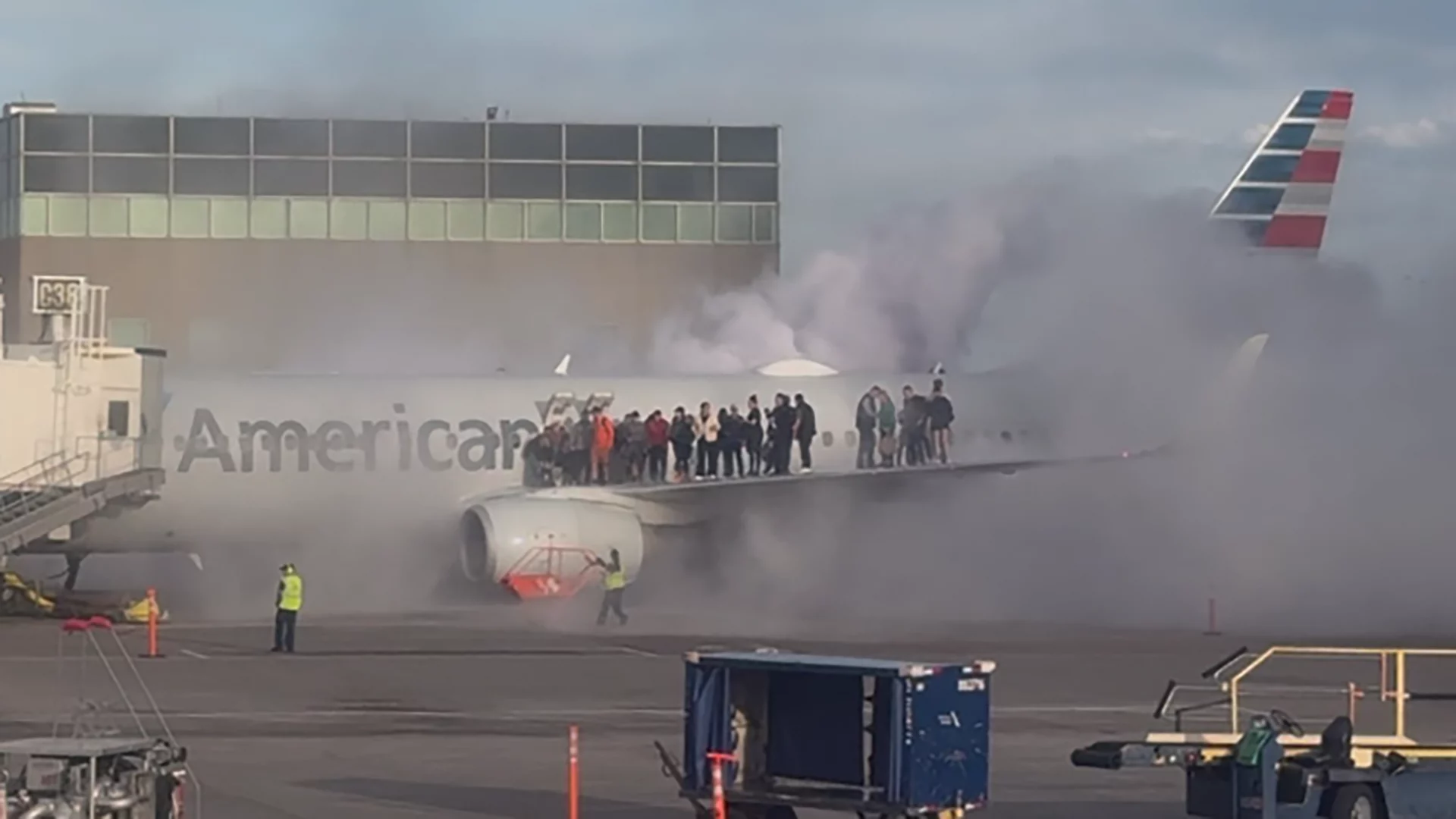 Pessoas na asa do avião com muita fumaça ao redor; abaixo, há fogo próximo à turbina