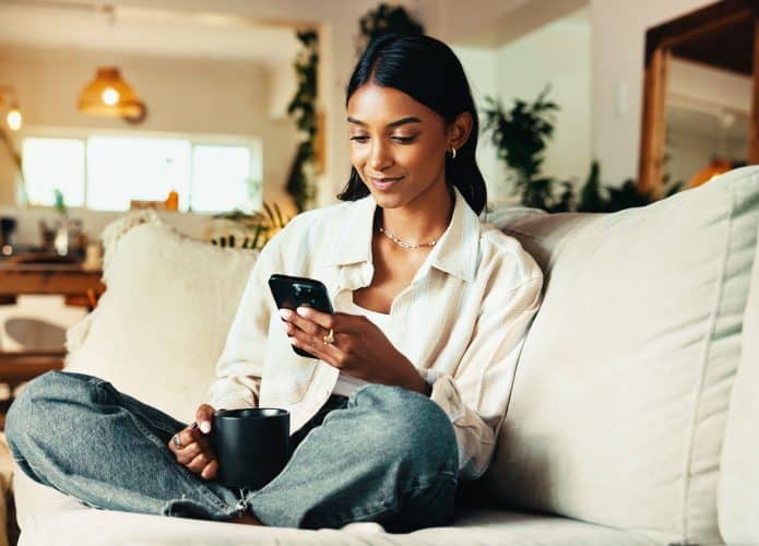 Mulher lendo e-book no smartphone sentada no sofá