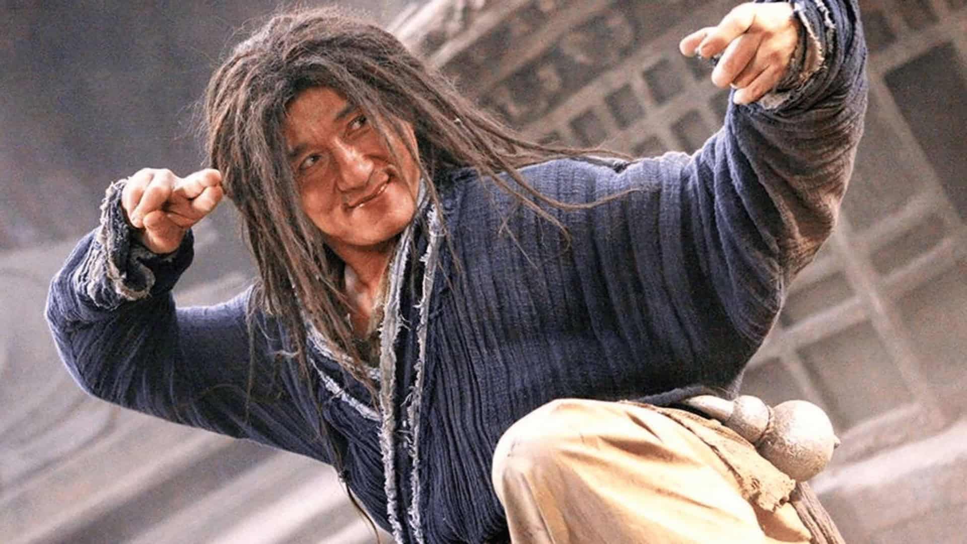Homem com cabelos desgrenhados, vestindo trajes rústicos e expressão determinada, em pose de combate em um cenário antigo
