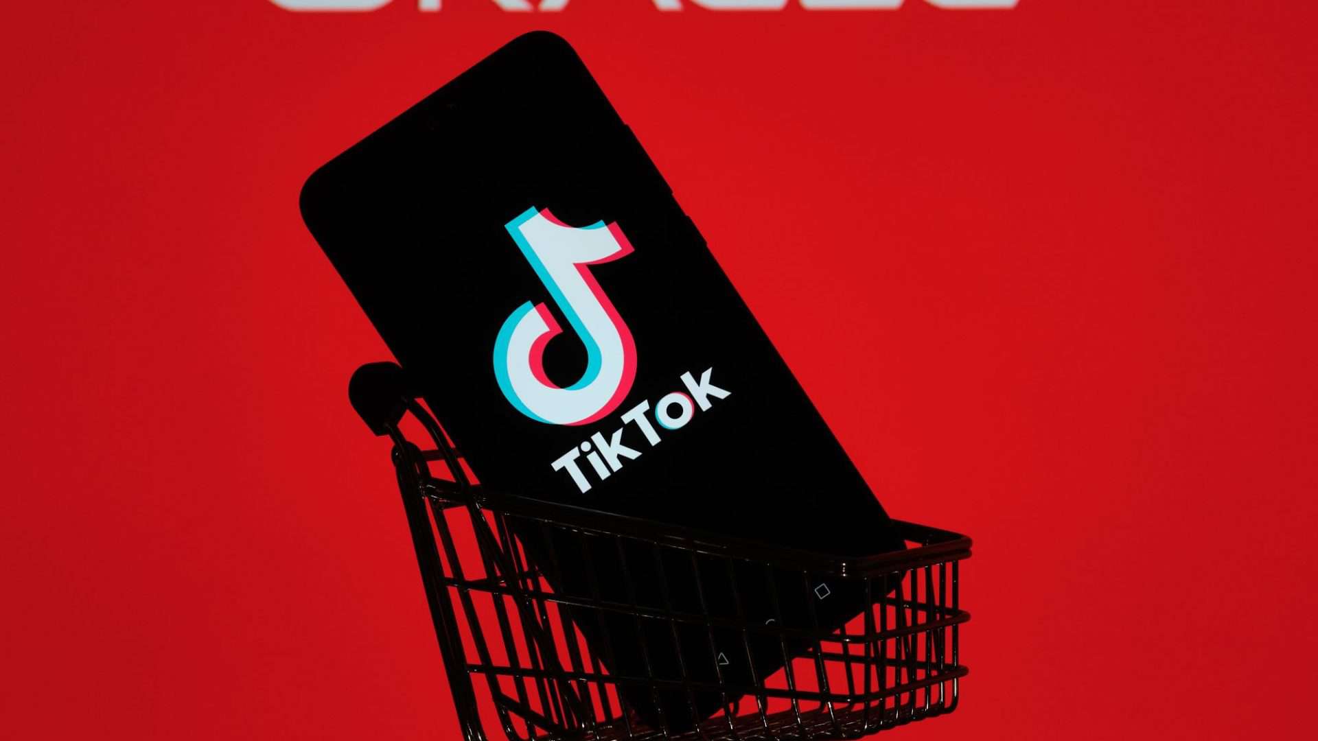 Ao fundo, logo da Oracle em uma tela vermelha; à frente, um smartphone em um mini-arrinho de compras com o logo do TikTok