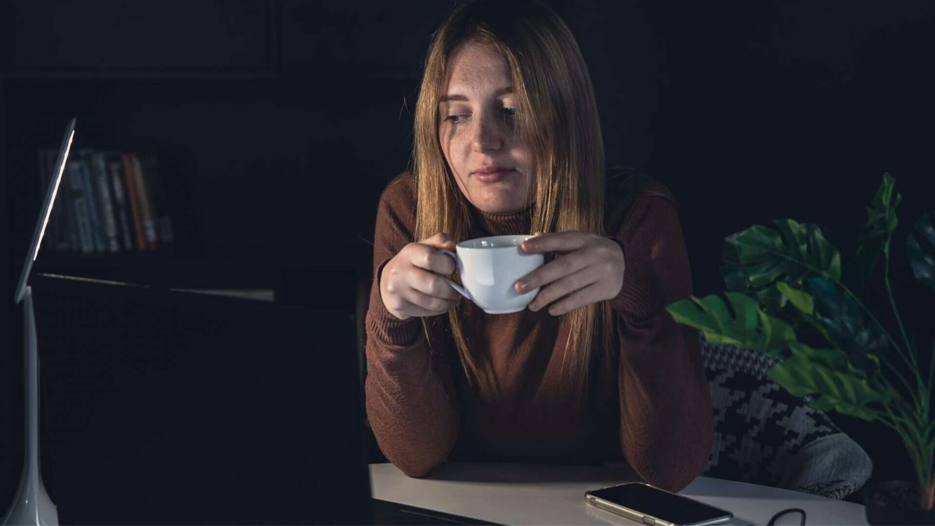 mulher com xícara de café em frente a um computador