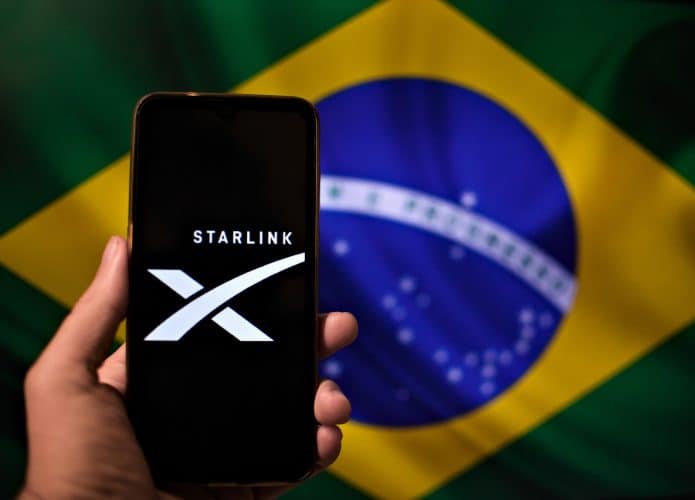 Logo da Starlink em um smartphone; ao fundo, bandeira do Brasil