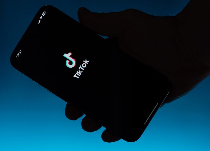 Logo do TikTok em um smartphone que está sendo segurado; ao fundo, um fundo azul