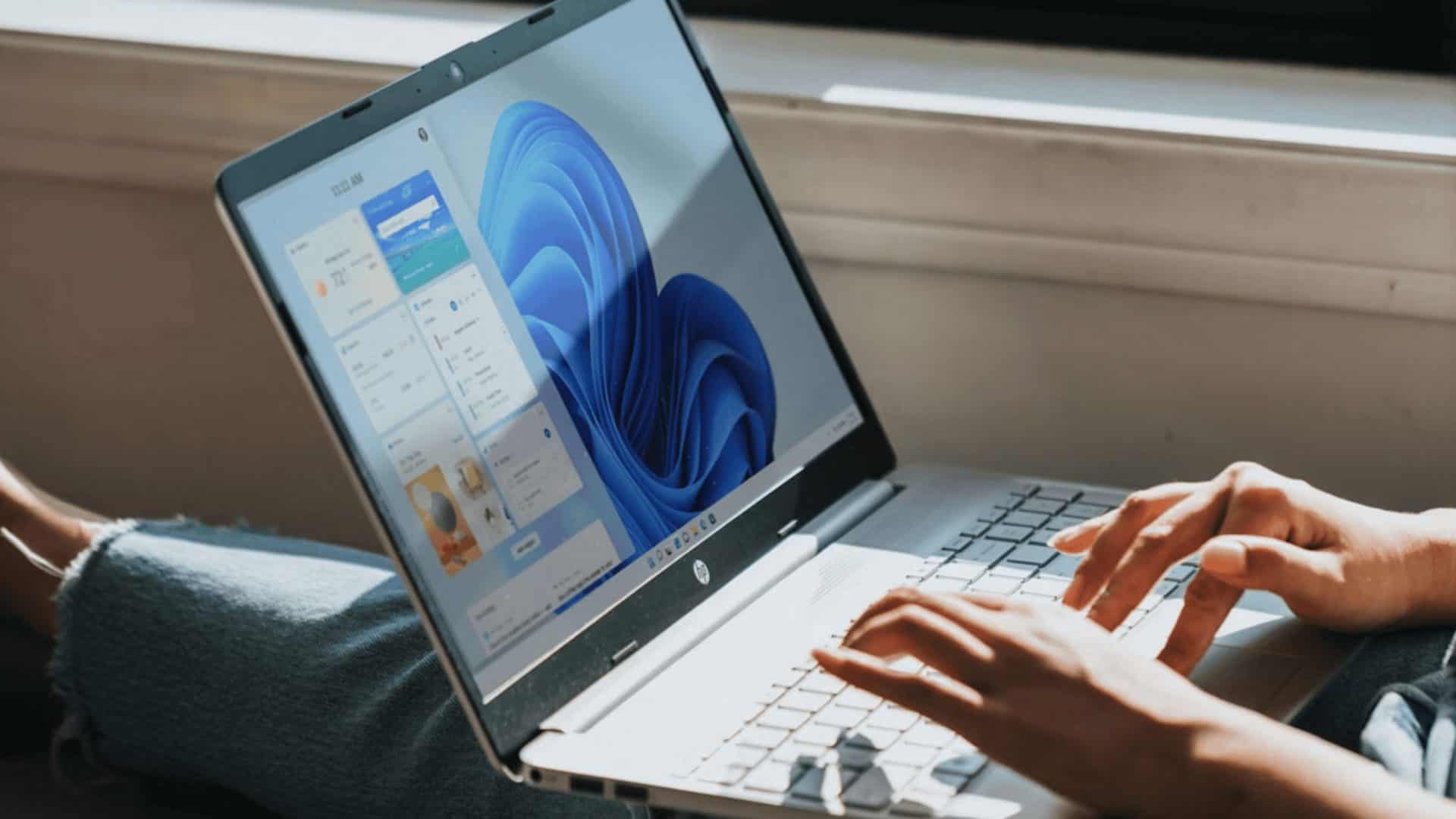 imagem mostra uma pessoa mexendo em um notebook com windows 11, sentado, ao lado de uma janela