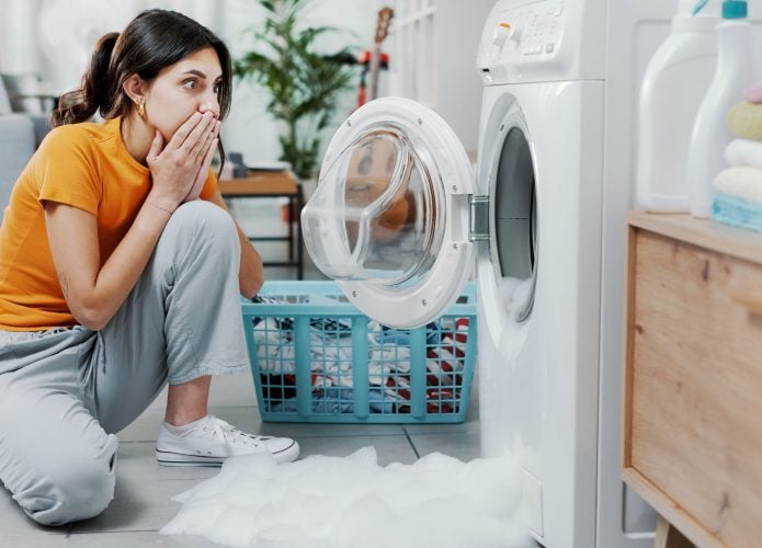Mulher verificando sua máquina de lavar danificada, o chão está alagado.