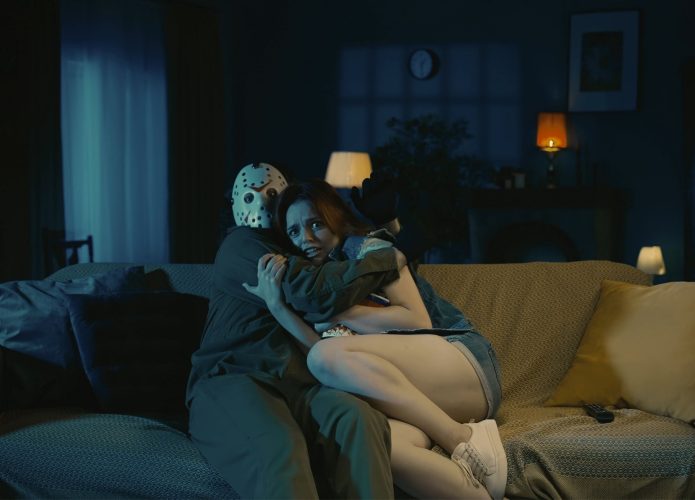 Homem horror maníaco sentado no sofá com uma garota, assistindo a um filme, abraçando um ao outro durante uma cena assustadora.