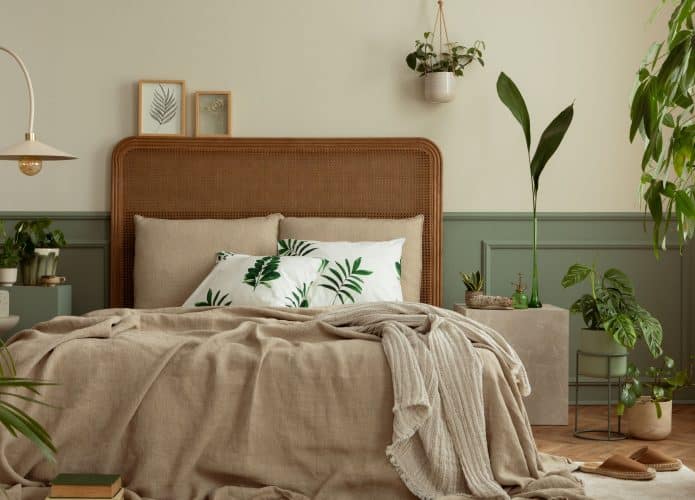 nterior de quarto quente e acolhedor com moldura de pôster simulada, cama boho, roupa de cama bege, parede verde com estuque, livros, chinelos marrons, plantas em vasos e acessórios pessoais. Decoração de casa. Modelo.