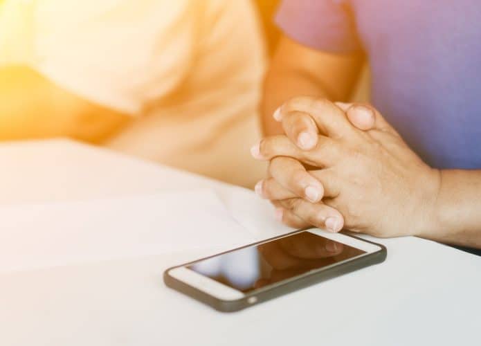 Homem orando sobre a Bíblia Sagrada em um Smartphone pela manhã antes de uma reunião. Mão de um adolescente com a Bíblia orando, mãos juntas em oração sobre uma Bíblia Sagrada na igreja, conceito de fé, espiritualidade e religião.