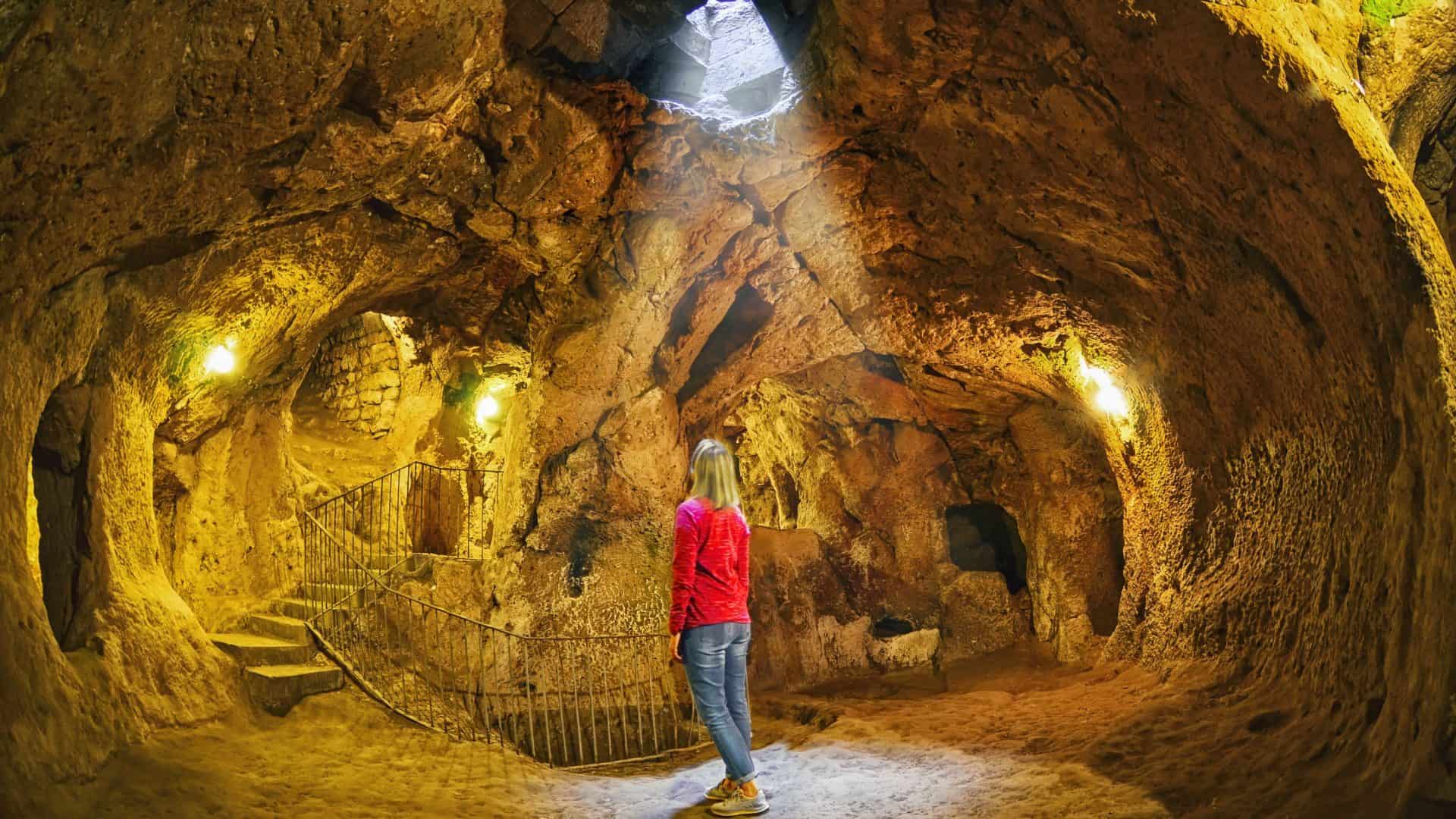 Derinkuyu caverna cidade subterrânea, Capadócia, Turquia .Fundo de viagem/ Mulher de jaqueta vermelha e calça jeans de costas na imagem.
