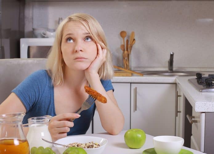 mulher comendo comida saudável na cozinha, à mesa. Desapontamento com a alimentação saudável, cansada de comer direito, cansada de fazer dieta. Escolha de nutrição adequada ou inadequada. A garota é obcecada por dietas.