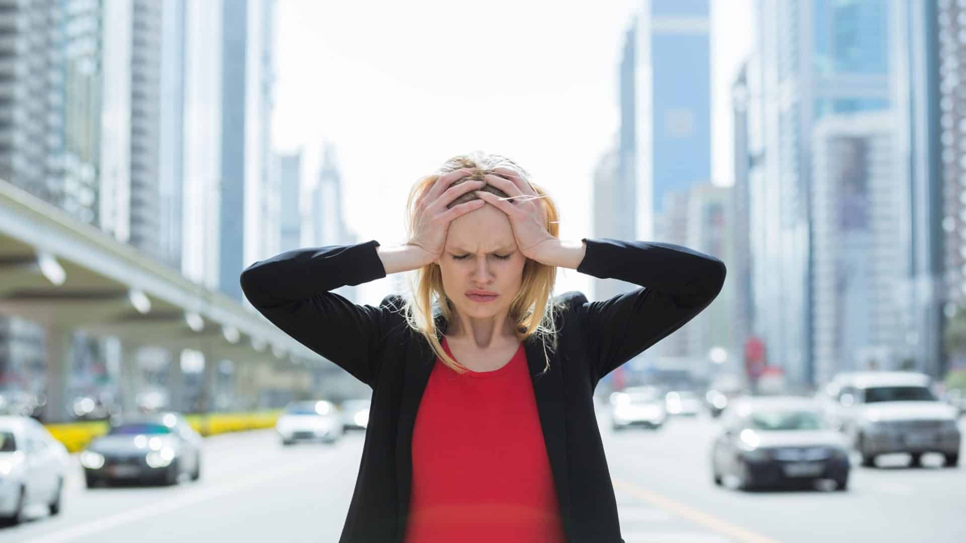 Mulher de negócios estressada na cidade movimentada. Mulher com as mãos na cabeça e trânsito de carros ao fundo.