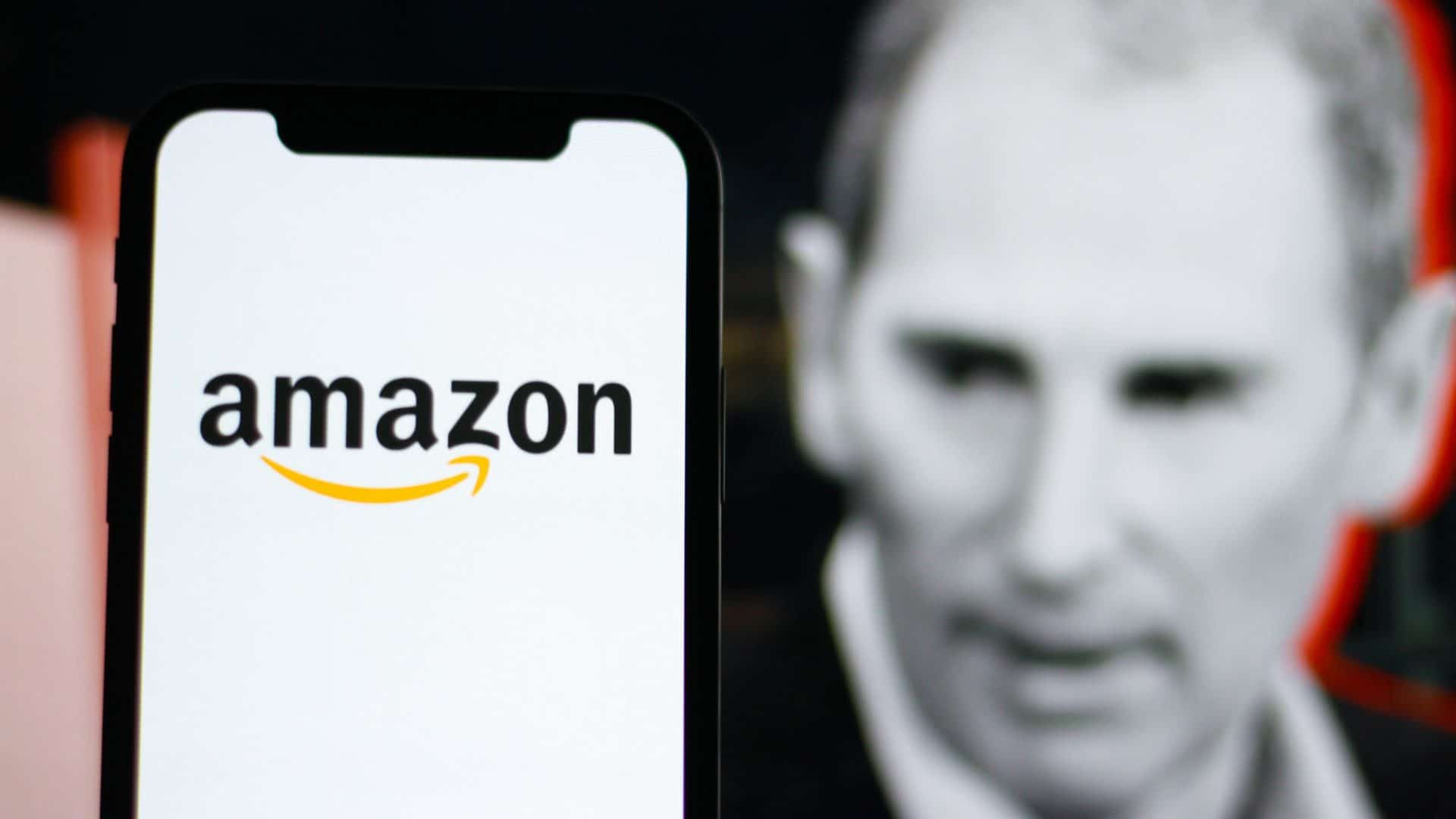 Celular com logomarca da Amazon na tela colocado na frente de monitor exibindo imagem em preto e branco, com contorno vermelho, do CEO da Amazon