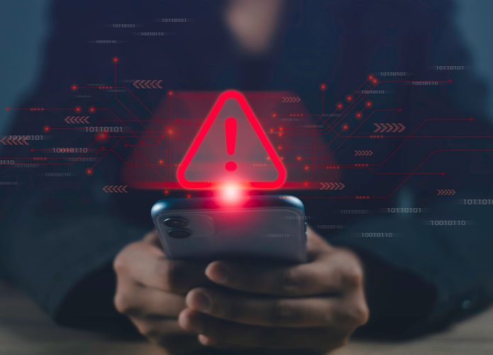 Pessoa usando celular com símbolo de atenção vermelho em cima dele