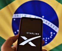 Pessoa segurando celular com logotipo da Starlink na tela na frente de bandeira do Brasil