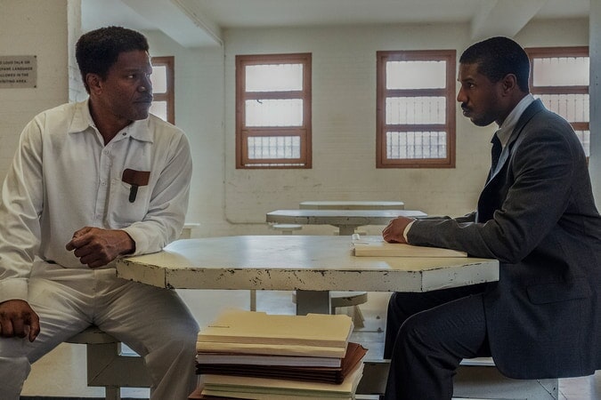 cena do filme mostra dois personagens sentados em uma mesa, conversando
