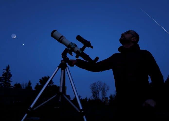 Astrônomo amador com seu telescópio olhando para o céu noturno.