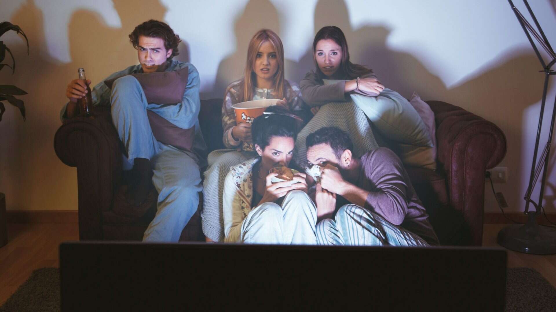 imagem mostra amigos adultos reunidos na sala de casa, assistindo a um filme de terror ação