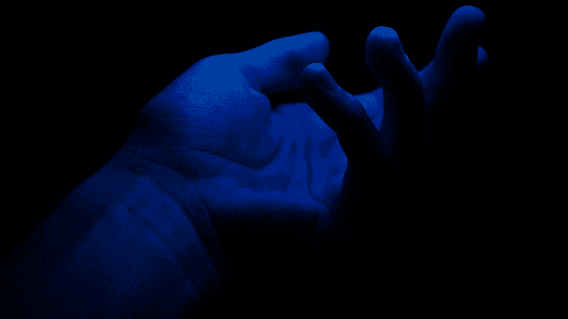 foto mostra uma mão em um ambiente escuro, mas iluminada por uma luz azul forte que deixa a pele azul