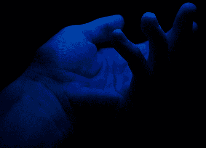 foto mostra uma mão em um ambiente escuro, mas iluminada por uma luz azul forte que deixa a pele azul