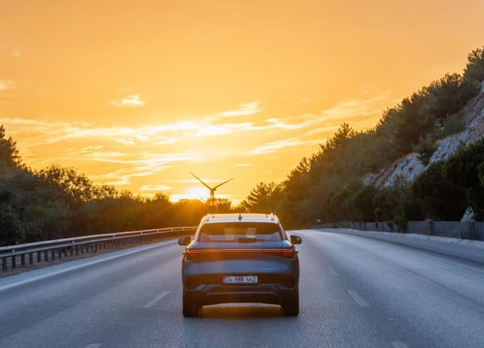 imagem mostra um carro elétrico da BYD rodando numa estrada vazia com o pôr-do-sol logo a frente