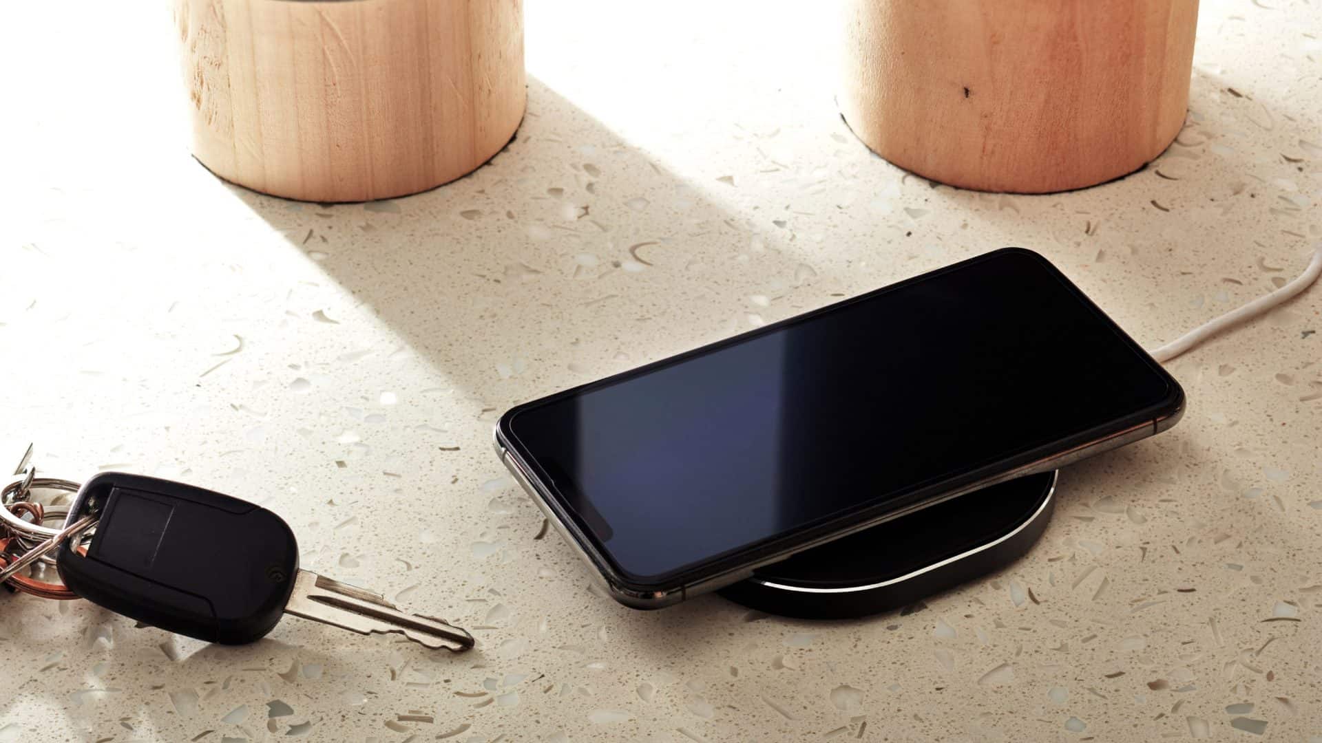 Um iPhone sendo carregado via indução ao lado de uma chave de carro