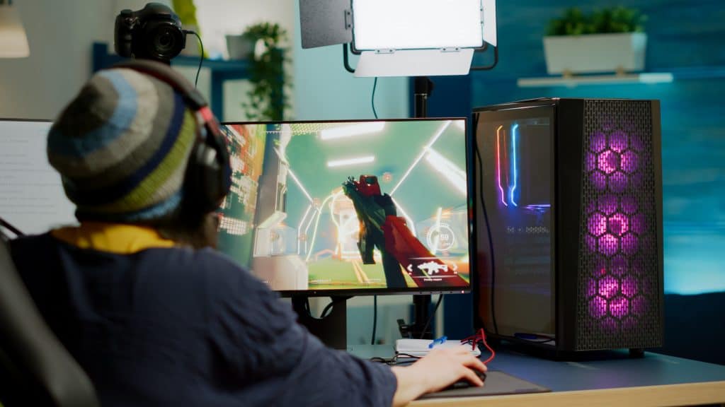 imagem mostra uma pessoa de costas para a câmera, jogando um game em um desktop/pc