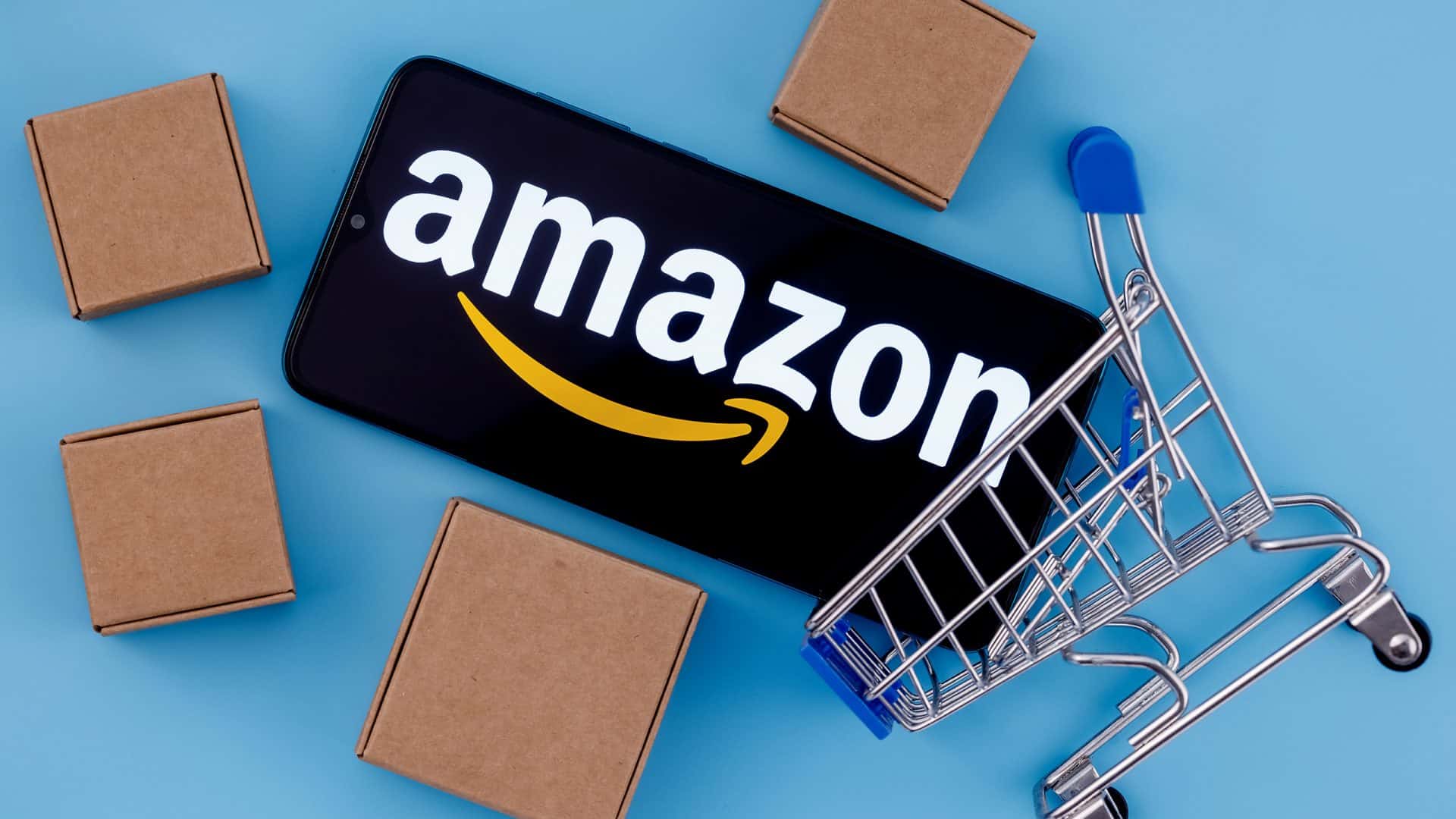 Logo da Amazon em um smartphone, que está em um mini carrinho de compras e duas mini caixas