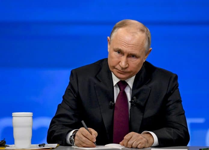 Vladimir Putin assinando um documento e olhando para frente