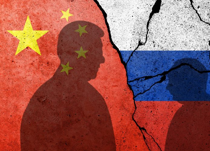 Bandeiras de China e Rússia ao fundo, projetadas em uma parede rachada; em primeiro plano, silhuetas de Xi Jinping e Vladimir Putin