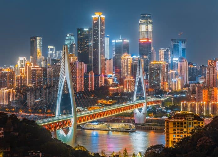 Paisagem urbana de Chongqing com arranha-céus iluminados e ponte sobre o Rio Yangtze à noite.