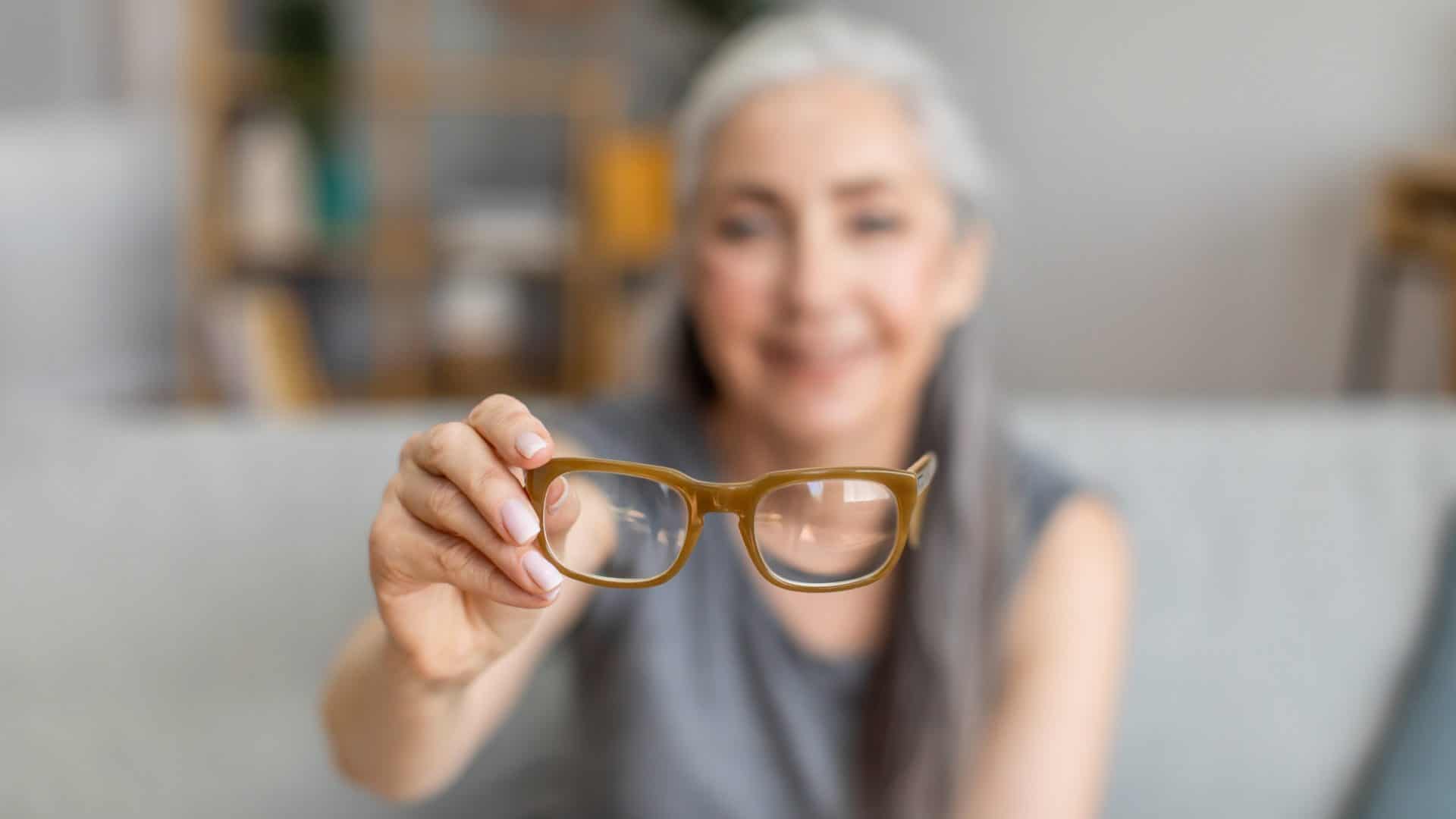 Mulher com óculos nas mão em fundo desfocado